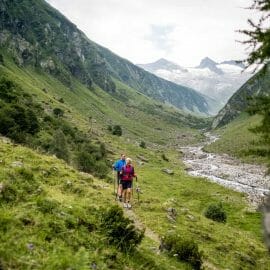 Turisté procházejí okolo horského potůčku mezi příkrými horami ve Wildkogel Areně