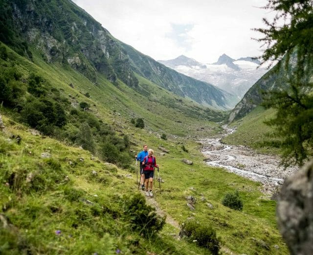 Turisté procházejí okolo horského potůčku mezi příkrými horami ve Wildkogel Areně
