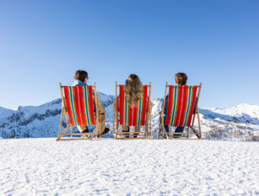Skitag in Zauchensee Tři lidé v pruhovaných židlích si užívají jaro na lyžích s výhledem na zasněžené vrcholky pod jasně modrou oblohou.