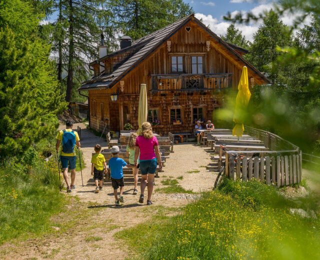 Rodina putuje k rustikální dřevěné chatě s venkovním posezením, která je ideální pro dovolená s dětmi.