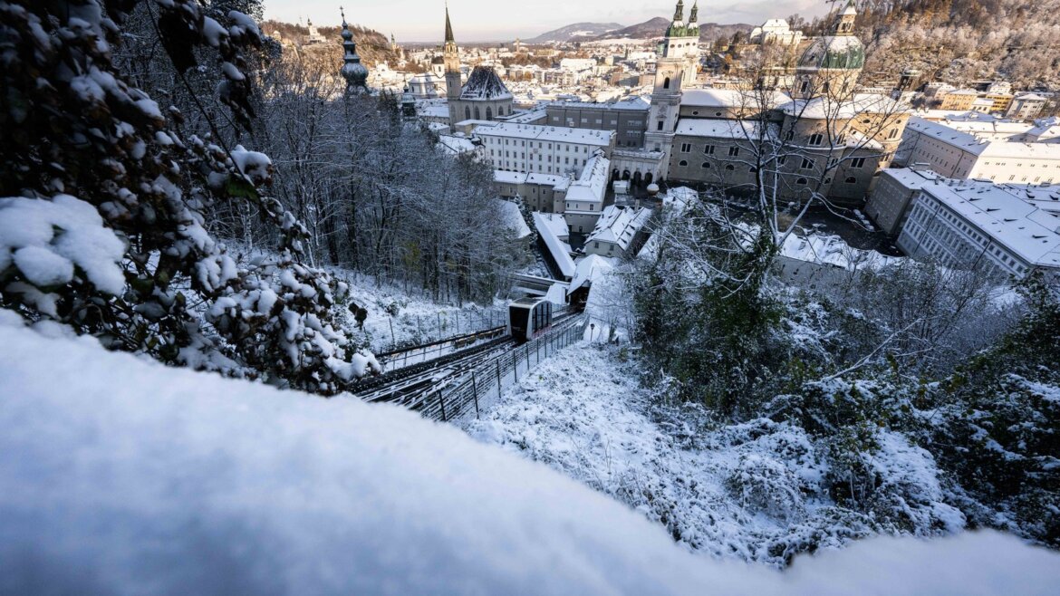 Zasněžený Salcburk, krajina s budovami, stromy a lanovou dráhou