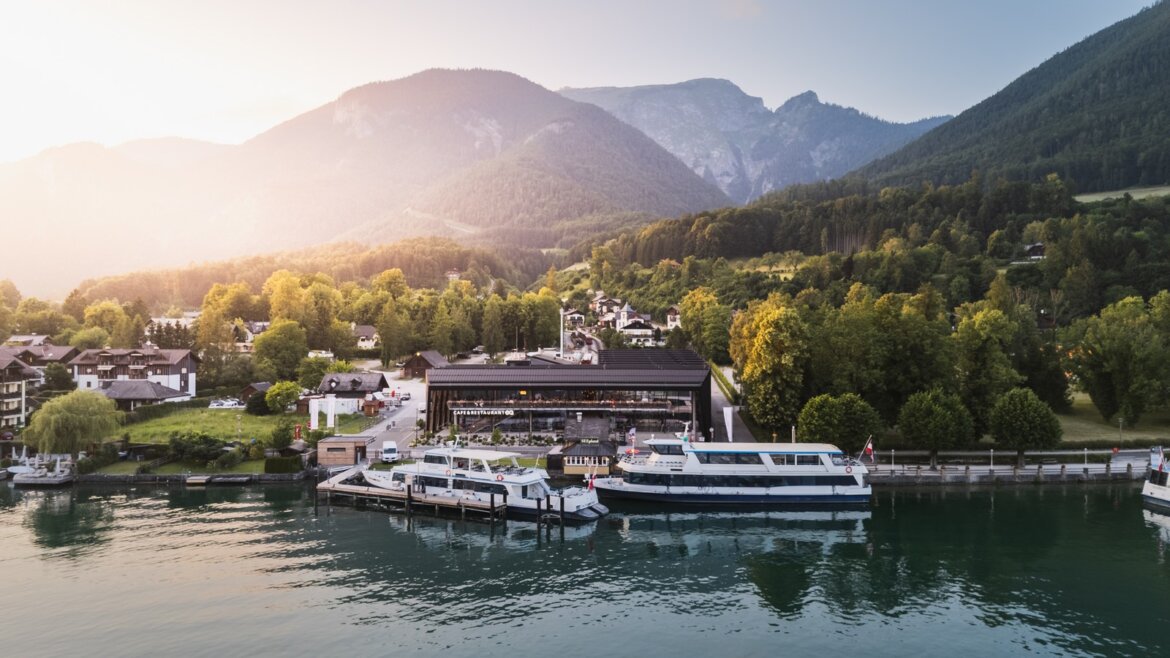 Lodě zakotvené v přístavu u jezera Wolfgangsee, dolní stanice zubačky na Schafberg a moderní restaurace ErlebnisQuartier při západu slunce (Zvětšený pohled)