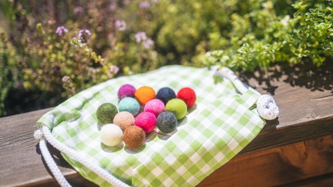 Barevné plstěné koule na zelené ginghamové tašce, ideální pro výlety za bylinkami v oblasti Hochkönig. (Zvětšený pohled)