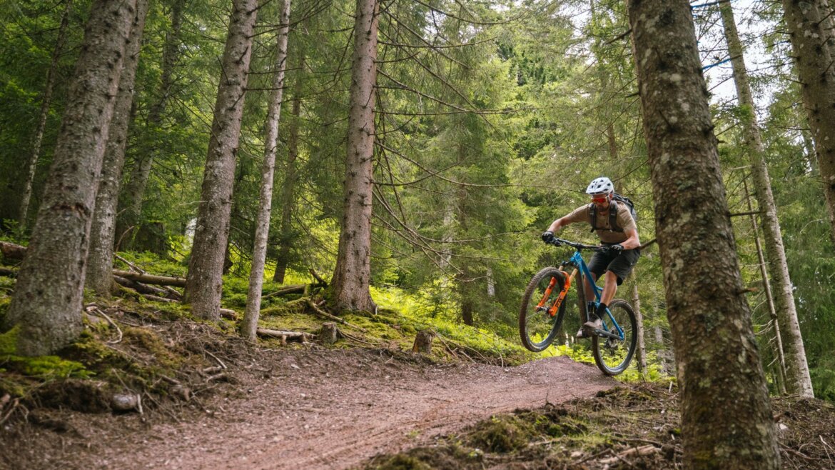 Horský cyklista jede a skáče na flowtrailu hustým lesem v oblasti Downhill Hochkönig.