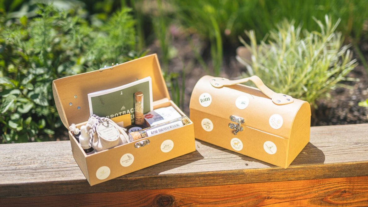 Dvě hnědé dárkové krabice leží na dřevěné římse venku poblíž zelených rostlin, ideální pro bylinky Hochkönig. (Zvětšený pohled)