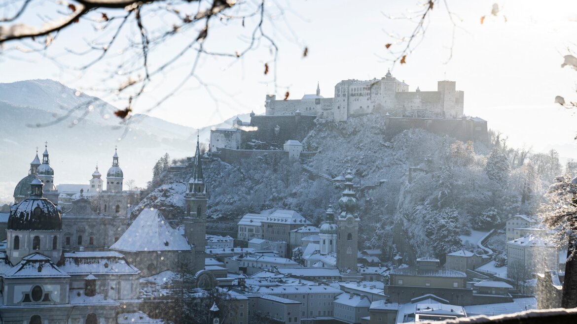 Zasněžená krajina Salcburku, top turistické cíle Salcburk a Solná komora, s pevností a kostelními kopulemi.