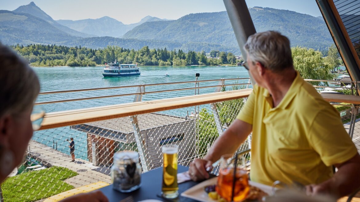 Restaurace EQ u Wolfgangsee © Salzburg AG Tourismus GmbH Dva lidé večeří u jezera a pozorují loď na Wolgangsee (Zvětšený pohled)