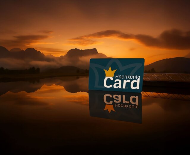 Karta Hochkönig Card stojí na zrcadlícím se jezeře při západu slunce, v pozadí jsou hory.