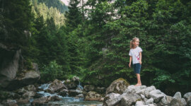 Dívka stojí na kamenech u potoka v Národním parku Vysoké Taury