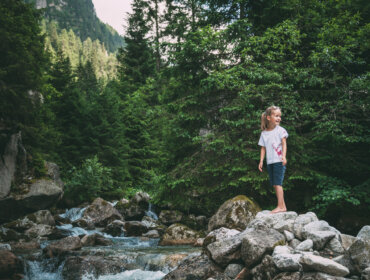 RS52_FNPHT4 © Ferienregion Nationalpark Hohe Tauern-lpr Dívka stojí na kamenech u potoka v Národním parku Vysoké Taury