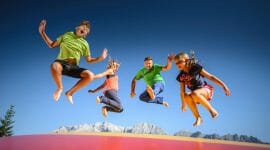 Děti a rodiče skáčou na obří trampolíně v zábavním parku pod širým nebem v horách Hochkönigu