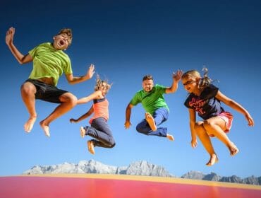 Děti a rodiče skáčou na obří trampolíně v zábavním parku pod širým nebem v horách Hochkönigu