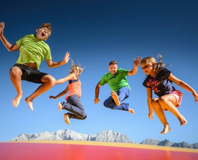 tonis-almspielplatz-3-1170×658 Děti a rodiče skáčou na obří trampolíně v zábavním parku pod širým nebem v horách Hochkönigu