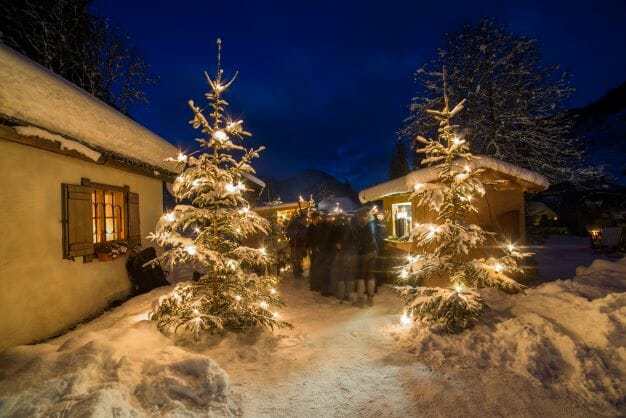 Stánky a ozdobené zasněžené stromy na tradičním vánočním trhu u poutního kostela Maria Kirchental v Salcburském Saalachtalu