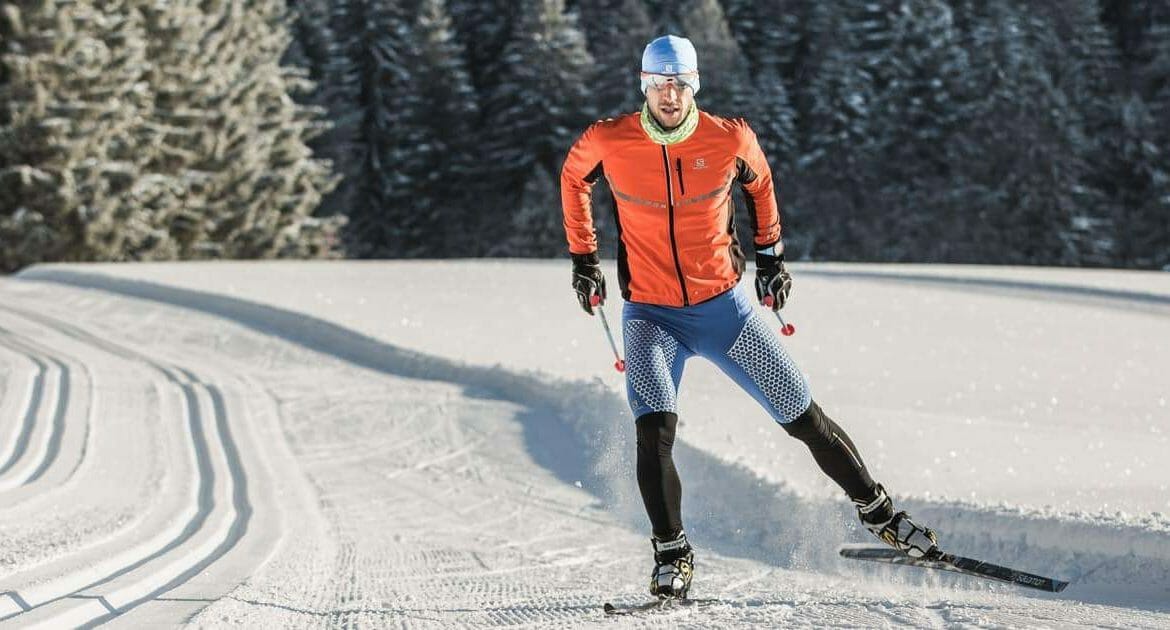 Běžkař na běžkách bruslí na upravené trati třpytivě bílým sněhem okolo zasněžených stromů