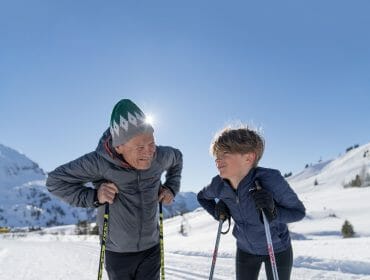 DSC03453_verlaengert Milovníci zimy: Starší muž a dítě na běžkách a usmívají se na zasněžené horské trase.