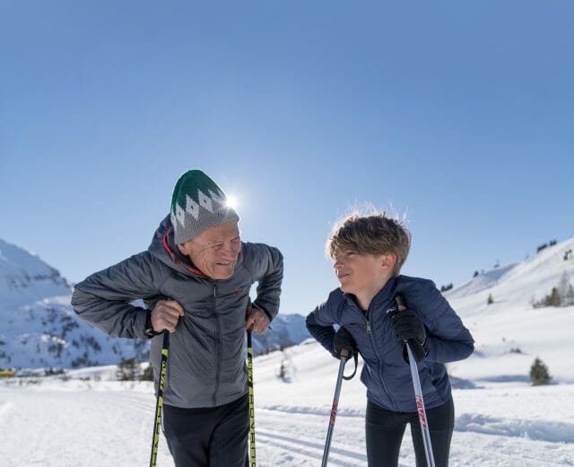 DSC03453_verlaengert Milovníci zimy: Starší muž a dítě na běžkách a usmívají se na zasněžené horské trase.