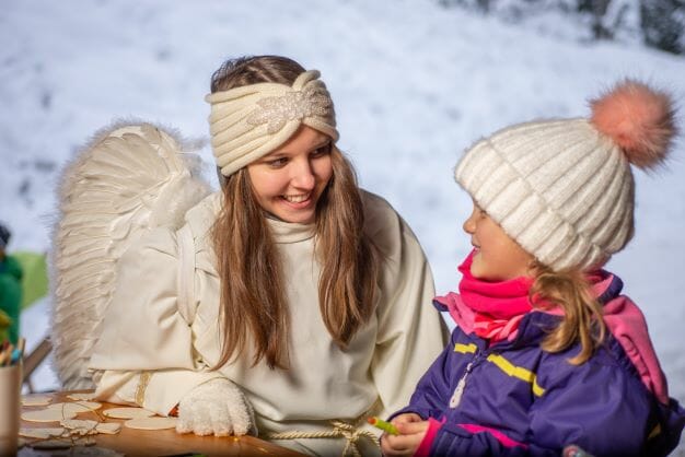 Dívka převlečená za anděla mluví na adventním trhu v Maria Kirchental v menší dívkou