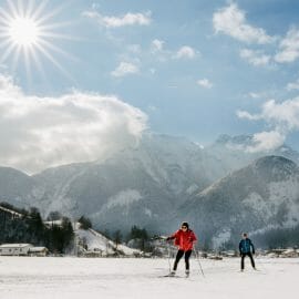 Pár projíždí upravenou běžkařskou stopou v údolí Salcburského Saalachtalu s majestátními vrcholy hor za zády