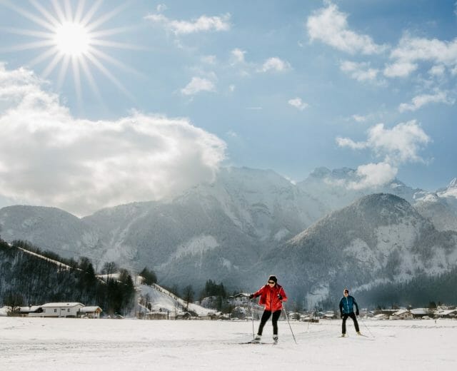 Pár projíždí upravenou běžkařskou stopou v údolí Salcburského Saalachtalu s majestátními vrcholy hor za zády