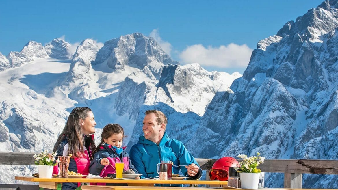Rodina svačí na slunečné terase uprostřed majestátních vrcholků hor v regionu Dachstein West