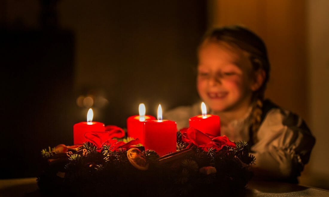 Adventní věnec se zapálenými červenými svíčkami je neodmyslitelnou součástí čtyř předvánočních týdnů