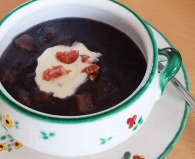 Polévka z červeného zelí v polévkovém hrnečku ozdobená lžící smetany a šunkou