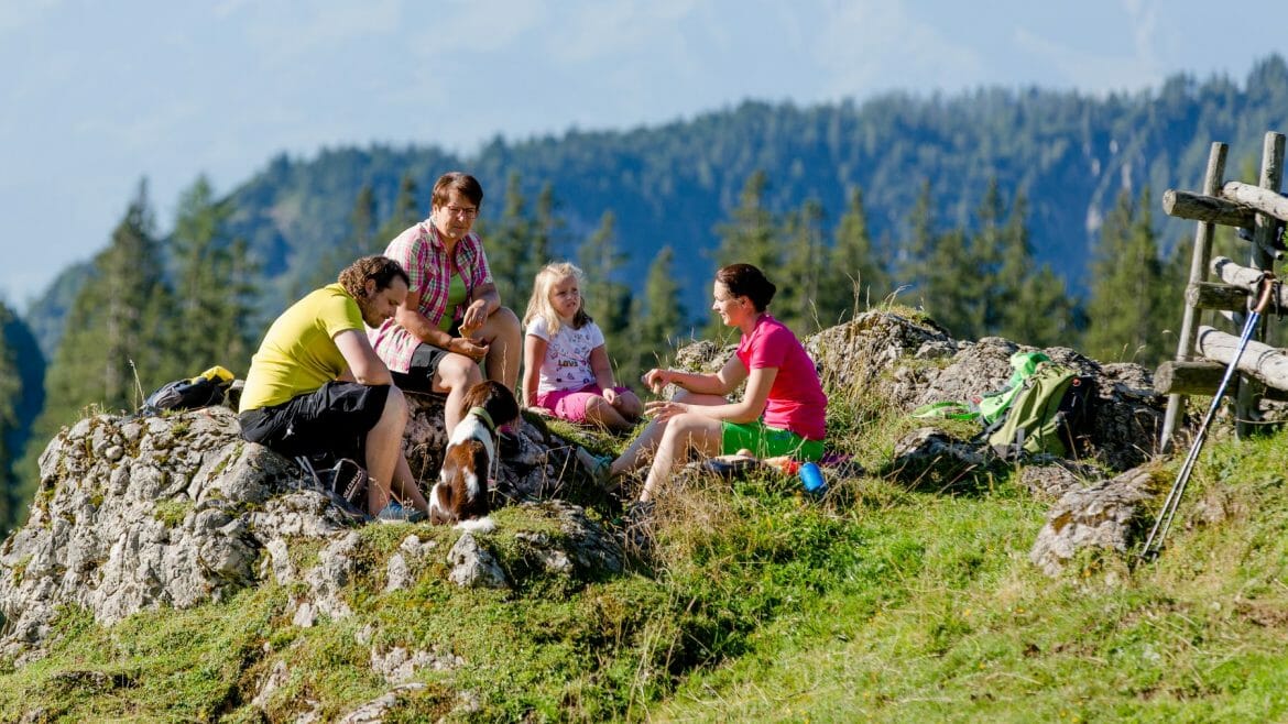 Rodina na výletě odpočívá na zelené pastvině v Přírodním parku Weissbach v Salcburském Saalachtalu