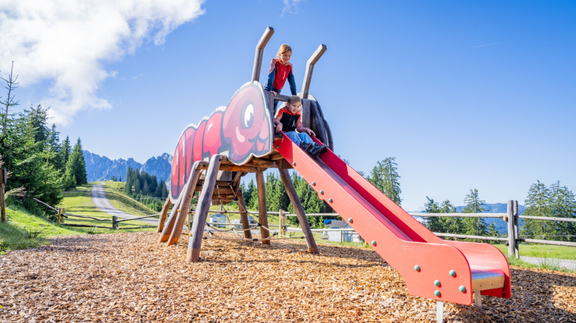 Dvě děti si hrají na červené skluzavce ve tvaru mravence v Dachstein West v horském světě medvěda Bruna