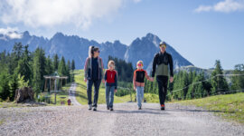 Čtyřčlenná rodina jde společně po štěrkové cestě během rodinné dovolené v Dachstein West.