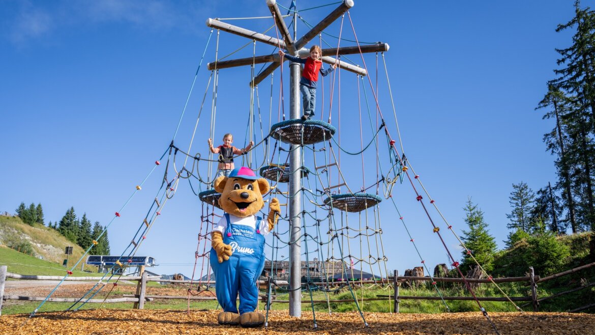 Dvě děti lezou po lanové prolézačce na venkovním hřišti s medvědem Brunem na Hornspitzu v Dachstein West