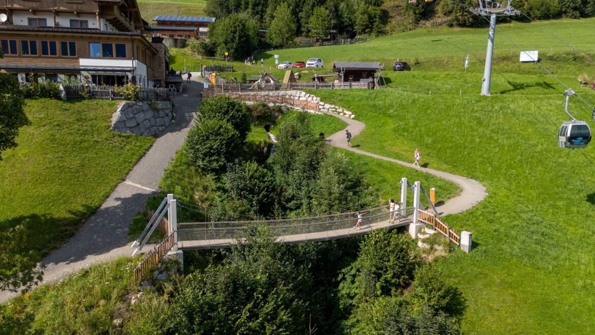 Malý most pro pěší překračuje zelenou rokli v travnaté krajině Léto Wildkogel-Arena Neukirchen Bramberg. (Zvětšený pohled)