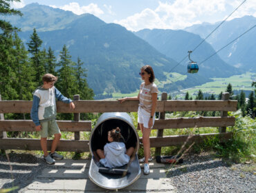 DSC04174 Tři děti na hřišti Léto Wildkogel-Arena Neukirchen Bramberg s výhledem na Alpy a lanovkou v pozadí.