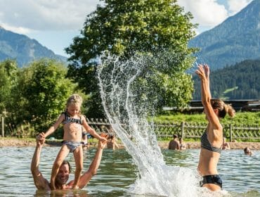 Rodina dovádí v jezírku ke koupání, obklopeném horami v Salcburském sportovním světě
