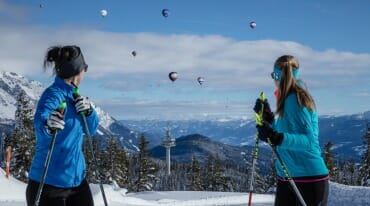 Běžkařky pozorují z vysokohorské běžecké tratě na hoře Rossbrand v oblacích balóny, které vzlétají z Filzmoosu