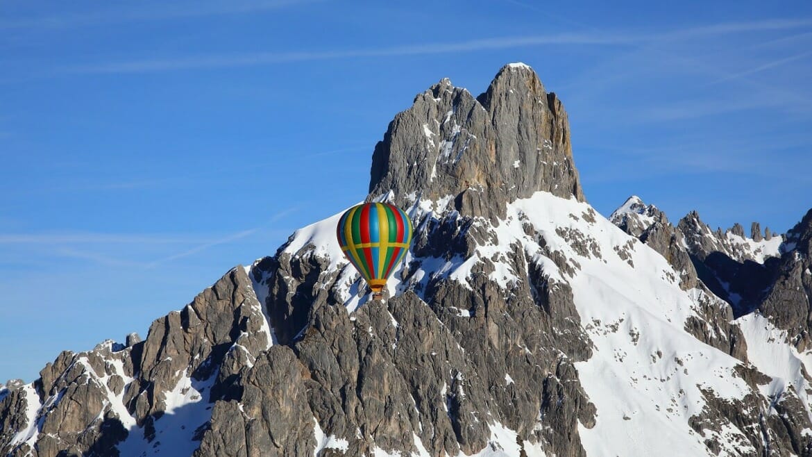 Barevný horkovzdušný balon se vznáší před kulisou štítů hory Bischofsmütze nad Filzmoosem