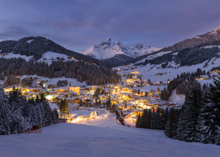 Filzmoos während der blauen Stunde Panorama zimního zasněženého Filzmoosu s osvětleným městem a sjezdovkami během