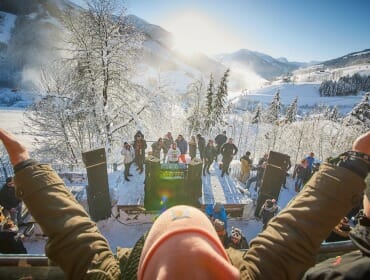 Dav lidí si užívá zasněžený venkovní koncert na Ski Openings Salcbursko, ruce zvednuté na oslavu pod sluncem.