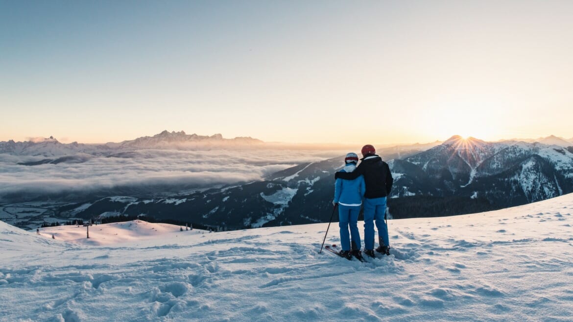 Pár na lyžích obdivuje západ slunce na sjezdovce