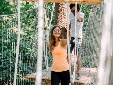 Dva lidé přecházejí přes lanový most v lese, užívají si sportovní aktivity v St. Johann v Salcbursku.