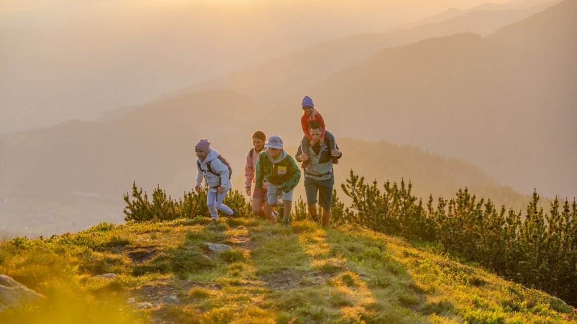 Letní turistika je pohodlnější díky lanovkám © Flachau Tourismus, Markus Berger Čtyři lidé se při východu slunce vydávají na travnatý kopec ve Flachau a užívají si výhled na hory a měkké zlatavé světlo. (Zvětšený pohled)