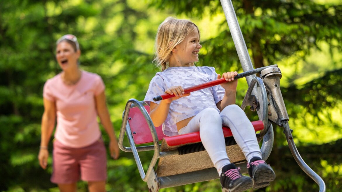 V horách čeká spousta zábavy © Flachau Tourismus, Markus Berger Usmívající se dítě na houpačce ve Flachau Salcbursko, v pozadí stromy a spokojený dospělý. (Zvětšený pohled)