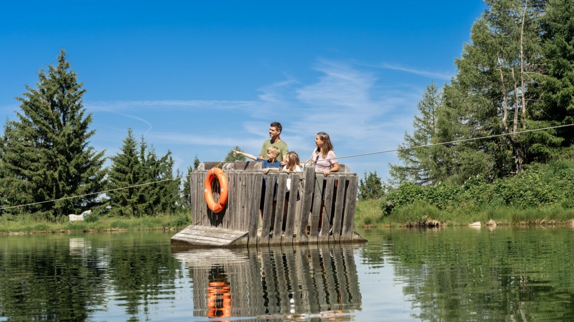 Vor na jezírku na Geisterbergu © JOsalzburg Rodina na dřevěném voru brázdí pod jasnou oblohou klidné jezero u Letních lanovek Svatý Jan v Salcbursku. (Zvětšený pohled)
