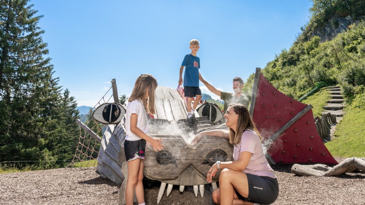 Některé atrakce na Geisterbergu mají i zvukové efekty © JOsalzburg Dvě děti a dospělí si hrají na sochu dračí hlavy - Rodinná dovolená sv. Jana léto, z jejíhož nosu se line pára. (Zvětšený pohled)
