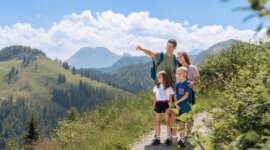 Čtyřčlenná rodina na horské stezce během rodinné dovolené v St. Johann a užívá si malebných výhledů.