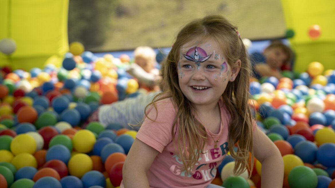 Usměvavá dívka s barvami na obličej si hraje v barevné kuličkové jámě - ideální pro Rodinná dovolená sv. Johanna léto.