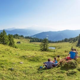 Turisté ve Flachau odpočívají na zelené horské louce Lackenalm a dívají se na hory