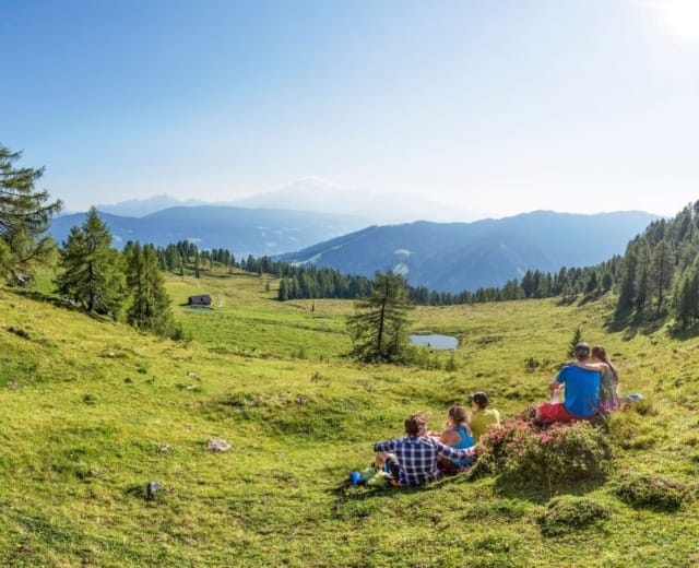 Turisté ve Flachau odpočívají na zelené horské louce Lackenalm a dívají se na hory