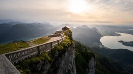 Dřevěný plot lemuje horskou cestu k chatě Himmelspforte s výhledem na jezera při západu slunce.