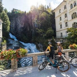 Cyklisté pozorují z mostu mohutný vodopád v centru města Bad Gastein
